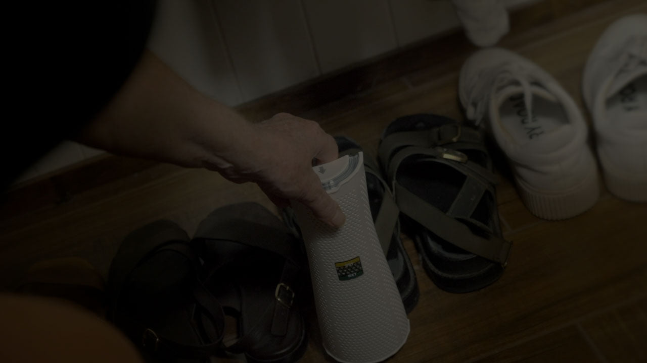 Person holding a white cylindrical object with text on a wooden floor with shoes in the background