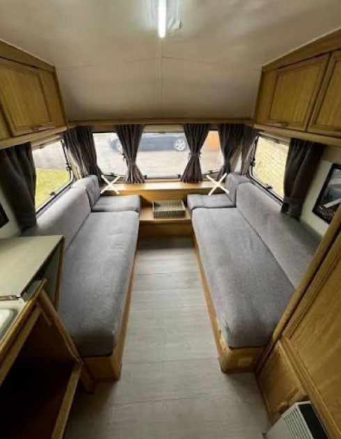 Interior of a compact living space with a sofa bed, wooden cabinets, and windows.