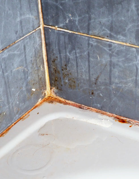 Close-up of a corner where a tiled floor meets a white baseboard with visible grime and dirt.