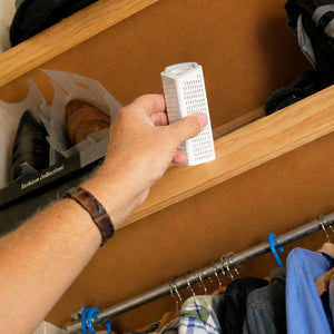 Hand holding a small white Dry Styx pod, with a clothing rack and clothes in the background.