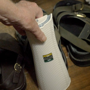 Person holding a white Dry Styx tower with a logo, surrounded by shoes on a wooden floor.
